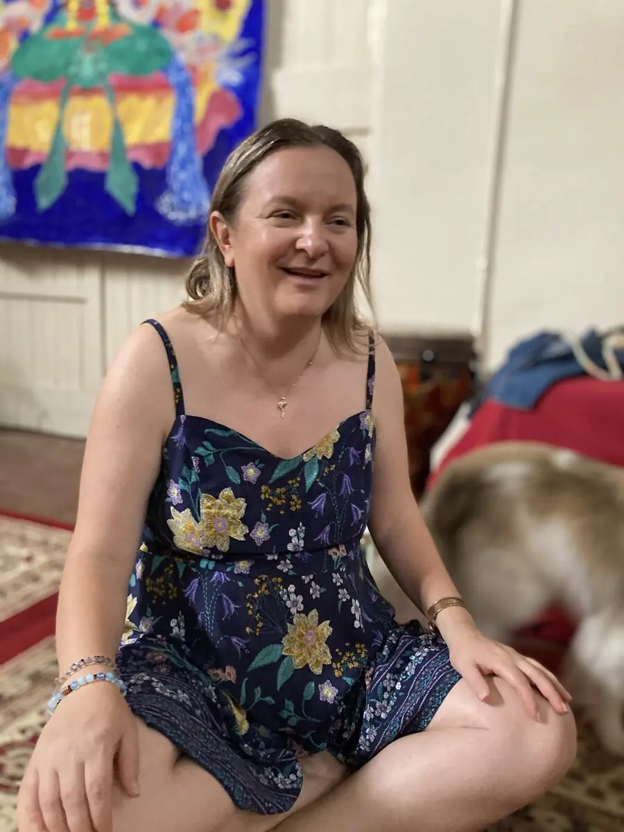 A person seated cross-legged, smiling in soft light