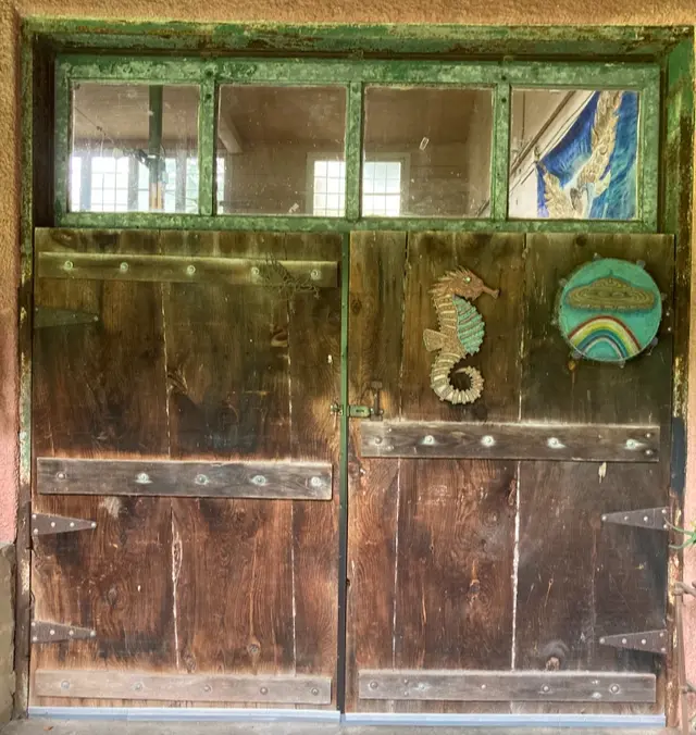 The old creamery's weathered wooden door, painted green, hung with a rainbow mandala and a seahorse