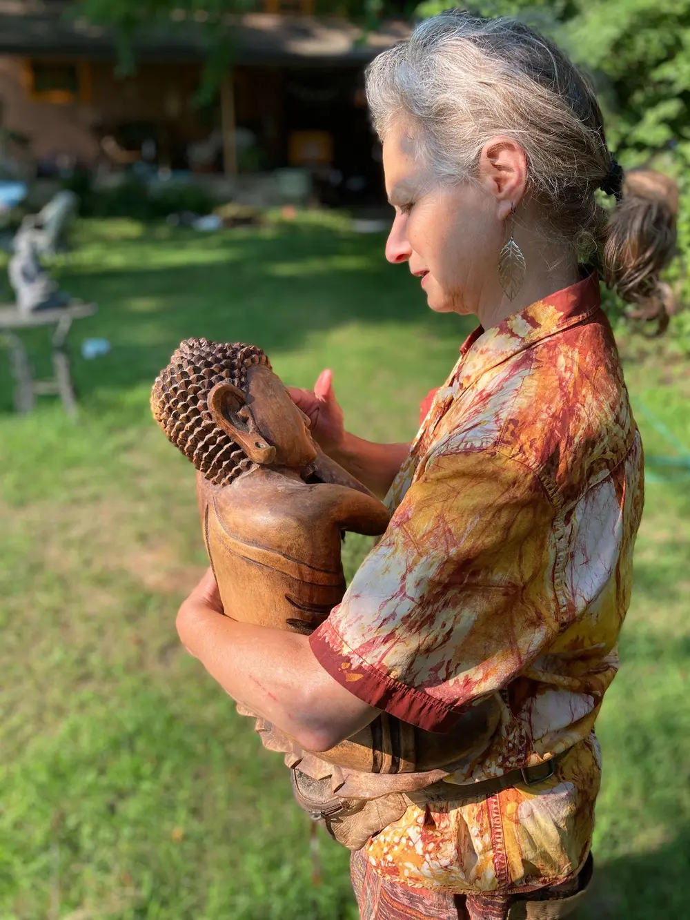 Dancing Leaf holding a small Buddha statue outdoors in a grassy garden