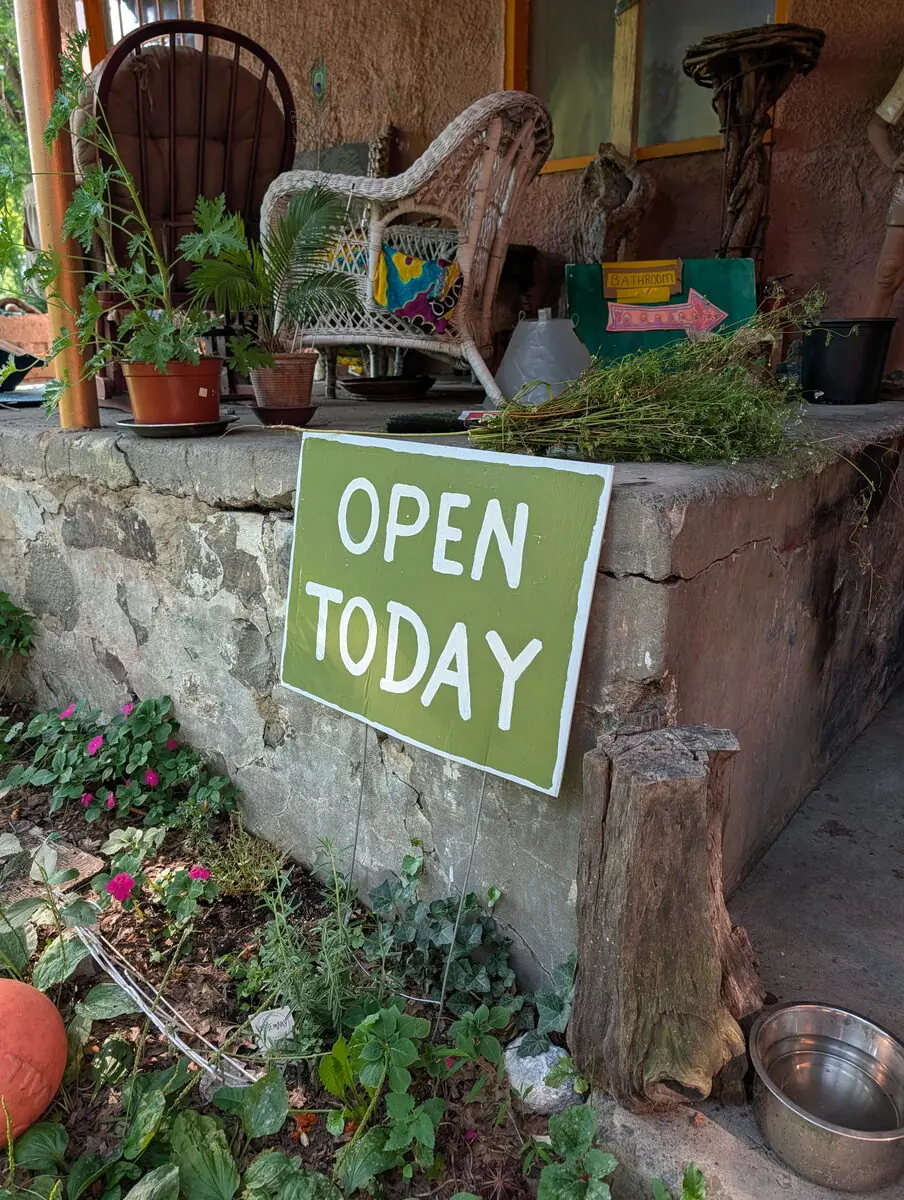 A rustic garden entrance with an open sign and flowering plants