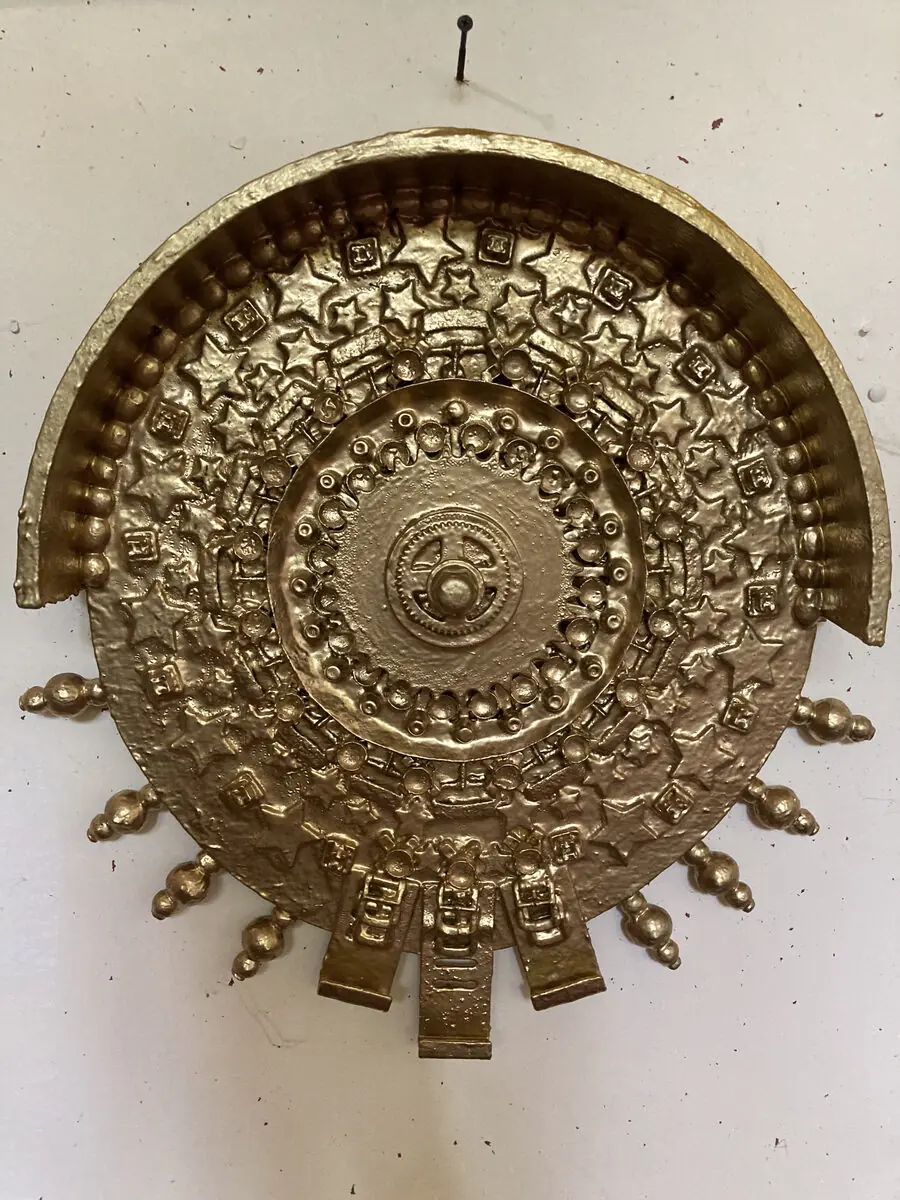 An ornate gold mandala hanging on a pale wall