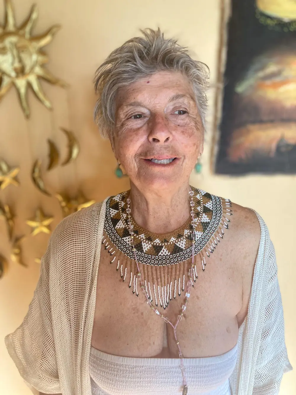 Michele, wearing layered jewelry and a light shawl, smiling warmly indoors