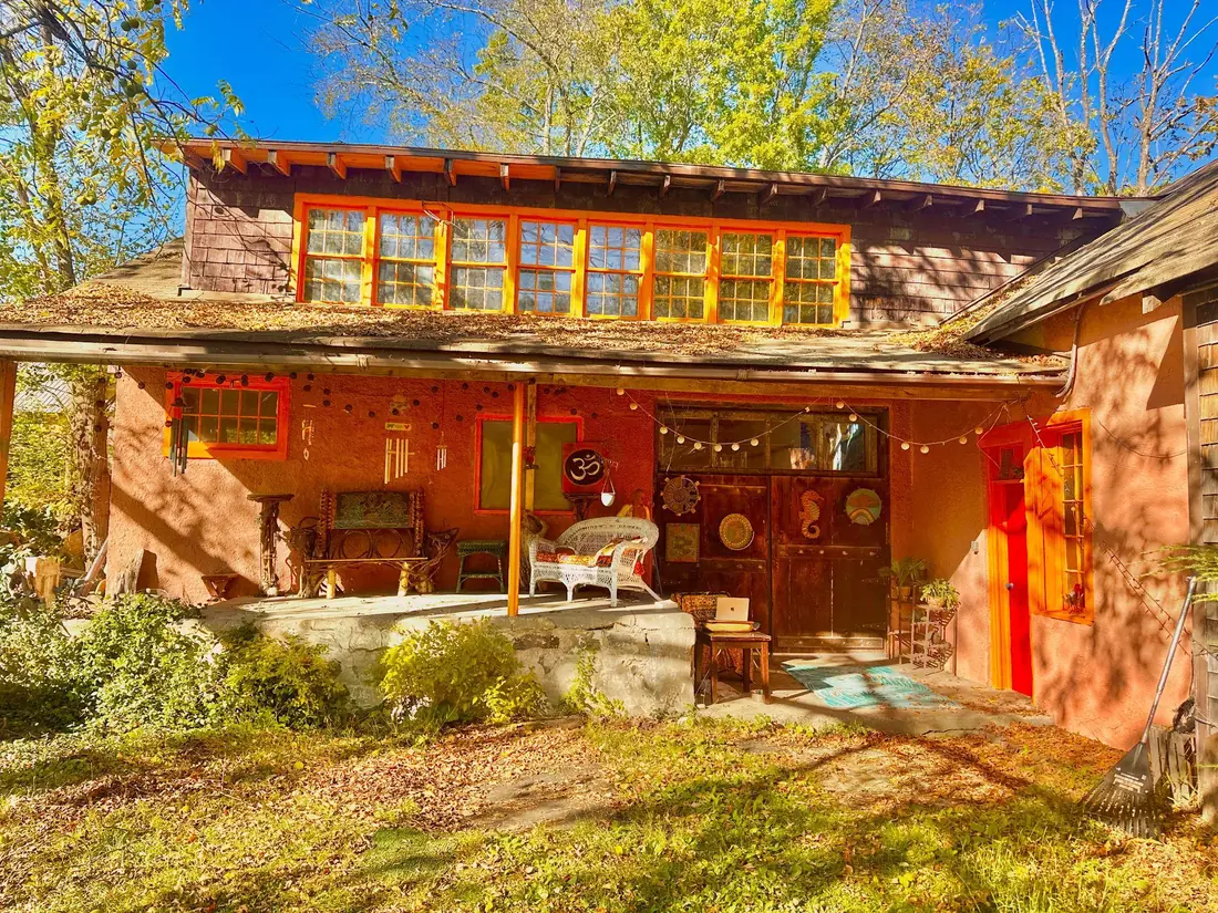 The Welcome Om sanctuary, a rustic, colorful building with a porch and garden in warm sunlight