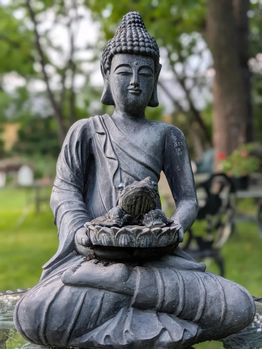 A seated Buddha statue holding an offering bowl in the sanctuary garden