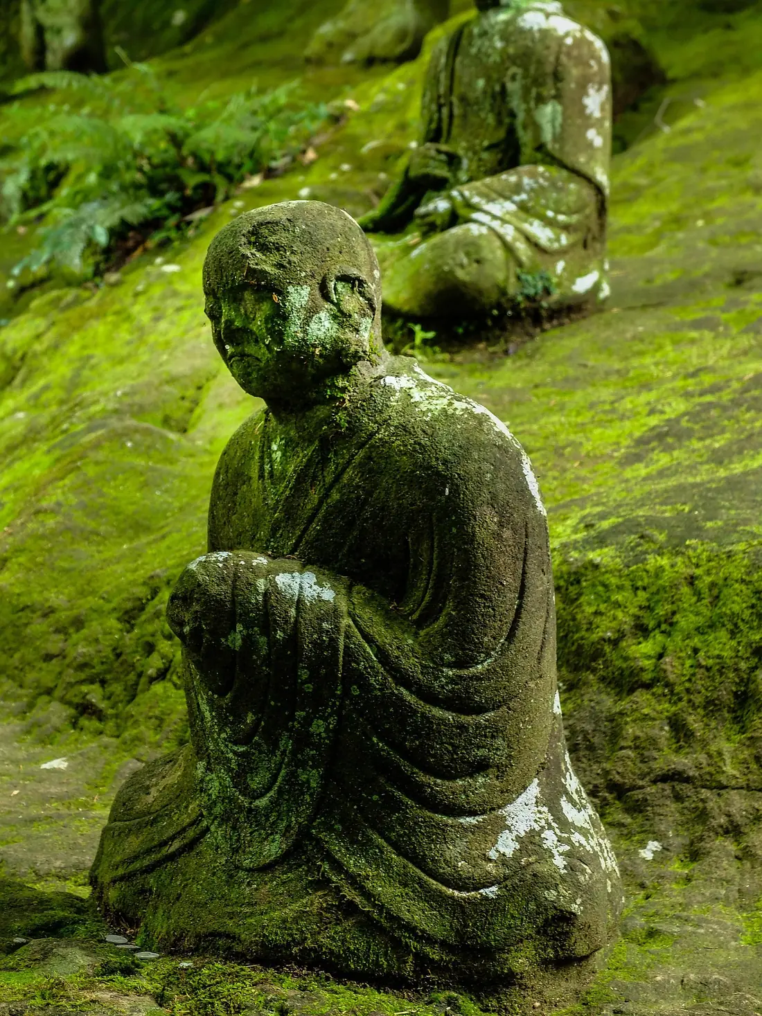 A moss-covered kneeling stone figure meditating in a lush green garden
