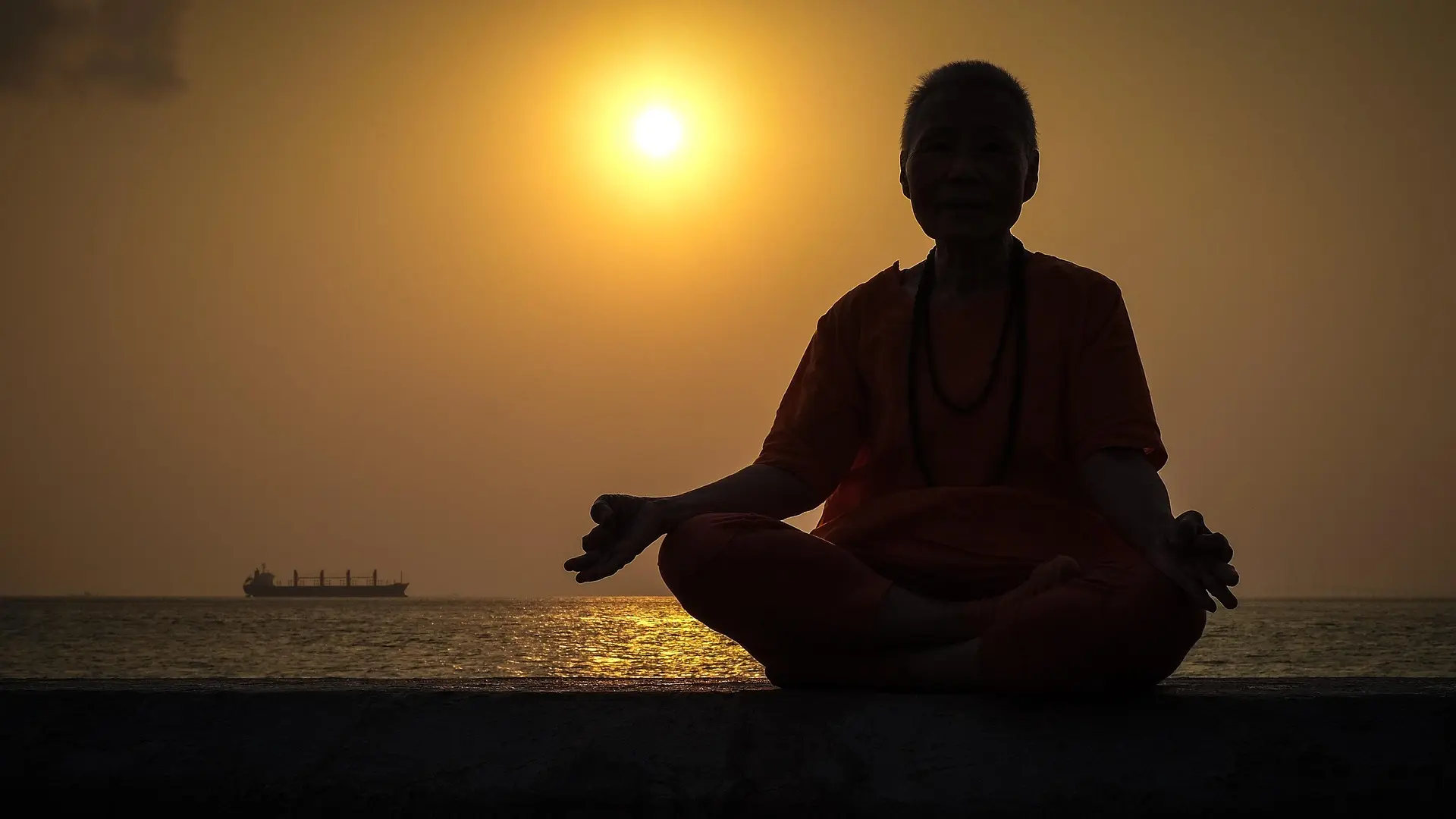 A silhouetted figure seated in meditation by the ocean as the sun rests on the horizon