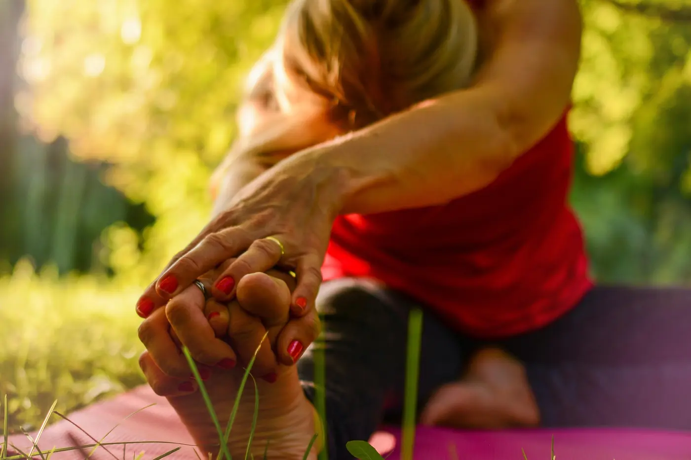 A close view of a hand reaching toward a foot in a seated stretch on a yoga mat